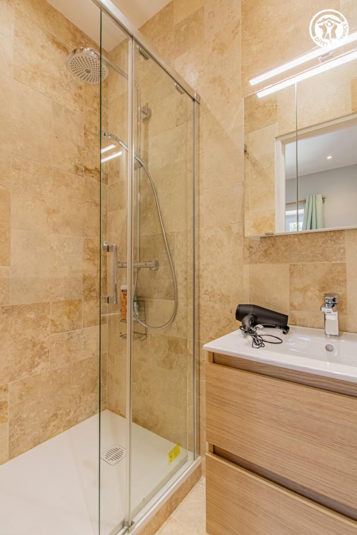 Un baño moderno con cabina de ducha de vidrio, tocador de madera con espejo y perchero.