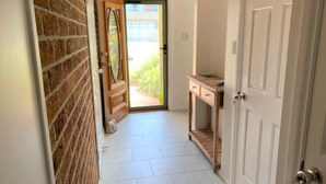 A hallway with a brick wall, a wooden door, and a tiled floor. - Shellharbour Beach Daze (Shellharbour)