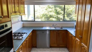 A kitchen with wooden cabinets, a stainless steel sink, and a dishwasher. - Shellharbour Beach Daze (Shellharbour)