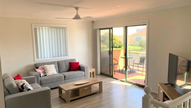 A spacious living room with a grey sofa, a wooden coffee table, and a TV on a wooden stand. - Shellharbour Beach Daze (Shellharbour)