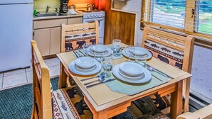 Een kleine keuken met een magnetron, fornuis en spoelbak. Een eettafel is gedekt met borden, glazen en bestek.