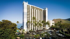Un grand hôtel à plusieurs étages, avec un parking et des palmiers.
