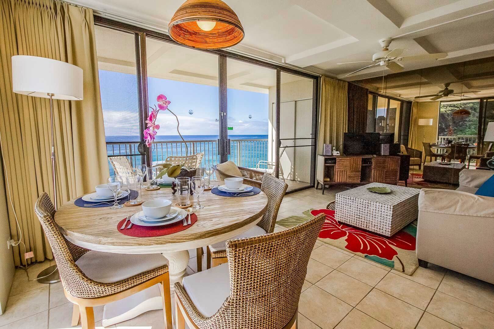 A dining area with a view of the ocean, a living room with a sofa and TV, and a balcony with curtains.