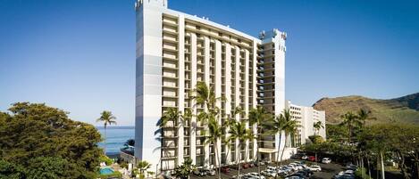A tall hotel with multiple floors, a parking lot, and palm trees.