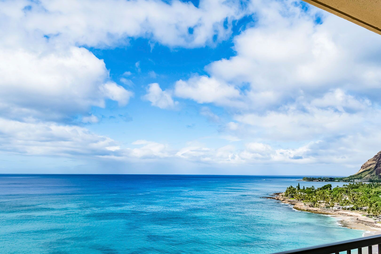 A coastal view with clear blue sea, a sandy beach, and a mountainous backdrop.