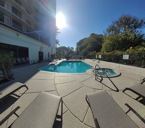A pool area with lounge chairs, a hot tub, and a building with balconies.