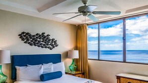Une chambre d’hôtel avec un lit, un ventilateur de plafond, une décoration murale représentant des poissons, une vue sur l’océan et une fenêtre avec des rideaux.