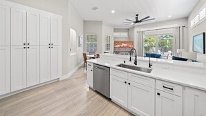 Una cocina moderna con armarios blancos, una isla central con un lavamanos y un ventilador de techo.