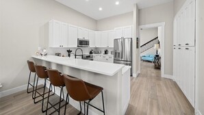 A modern kitchen with white cabinets, stainless steel appliances, and a central island with bar stools.