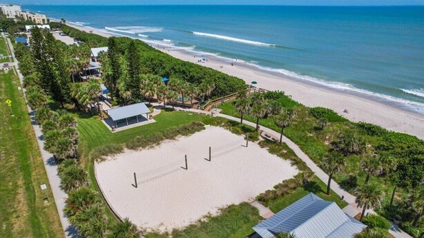 An aerial view of a beachside property with a large sandy area, pathways, and surrounding greenery.