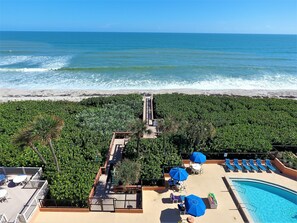 A rooftop pool area with lounge chairs and umbrellas, overlooking a beach and ocean. - Beachfront Condo w/ Pool & Balcony in FL (Indian Harbour Beach)