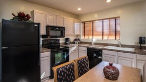 Una cocina moderna con armarios blancos, un refrigerador negro, un microondas, un horno y un lavavajillas. Hay una mesa de comedor con dos sillas y un jarrón decorativo.