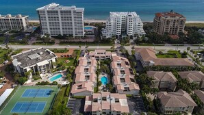 A high-rise hotel with multiple floors, a swimming pool, tennis courts, and a beach view.