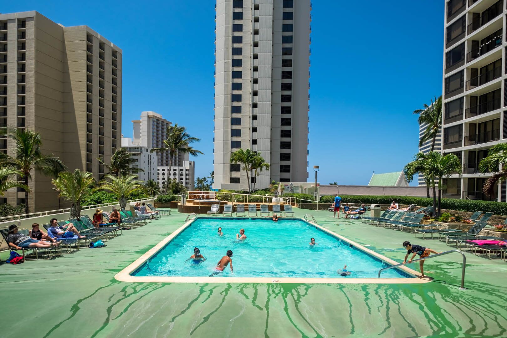 Zona de piscina con sillas de descanso y una piscina rodeada de edificios altos.