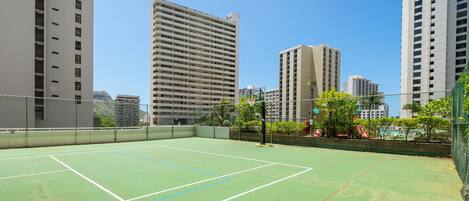 An outdoor tennis court surrounded by high-rise buildings.