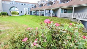 A residential building with multiple balconies, a well-maintained lawn, and flowering plants in the foreground. - Deluxe 1BR Condo w/ Jacuzzi & Bay Views (Newport)