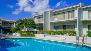 A hotel with a swimming pool, balconies with white railings, and a clear blue sky. - Beachside Rental w/ Balcony & Pool (Boca Raton)