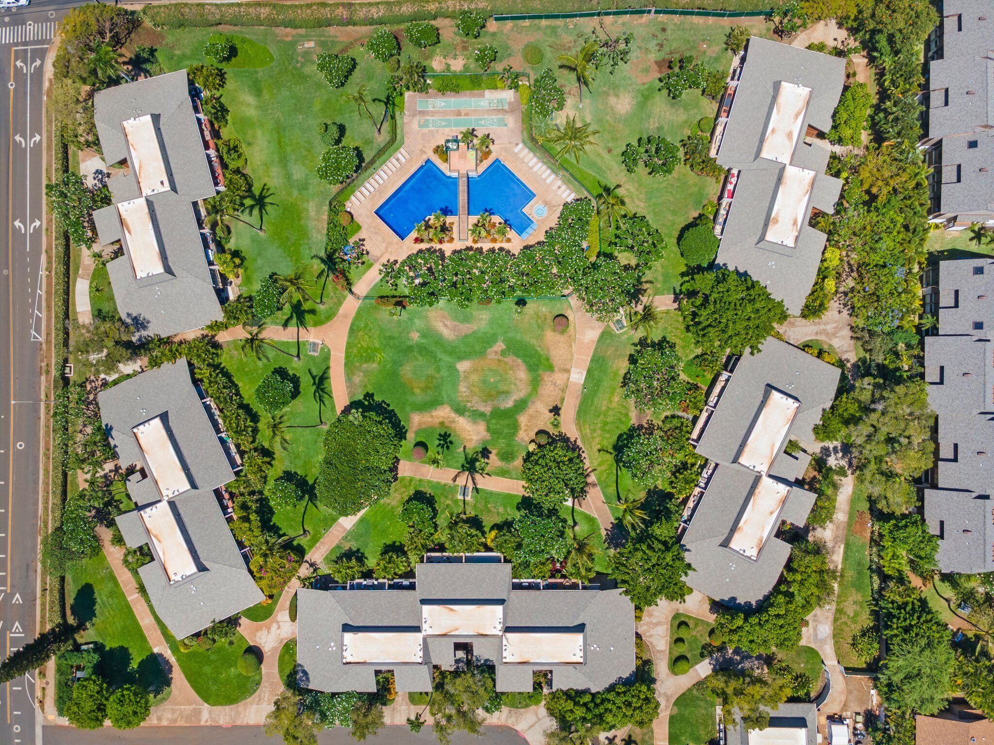 Vista aérea de un complejo residencial con varias edificaciones, una piscina central y céspedes y árboles bien cuidados.