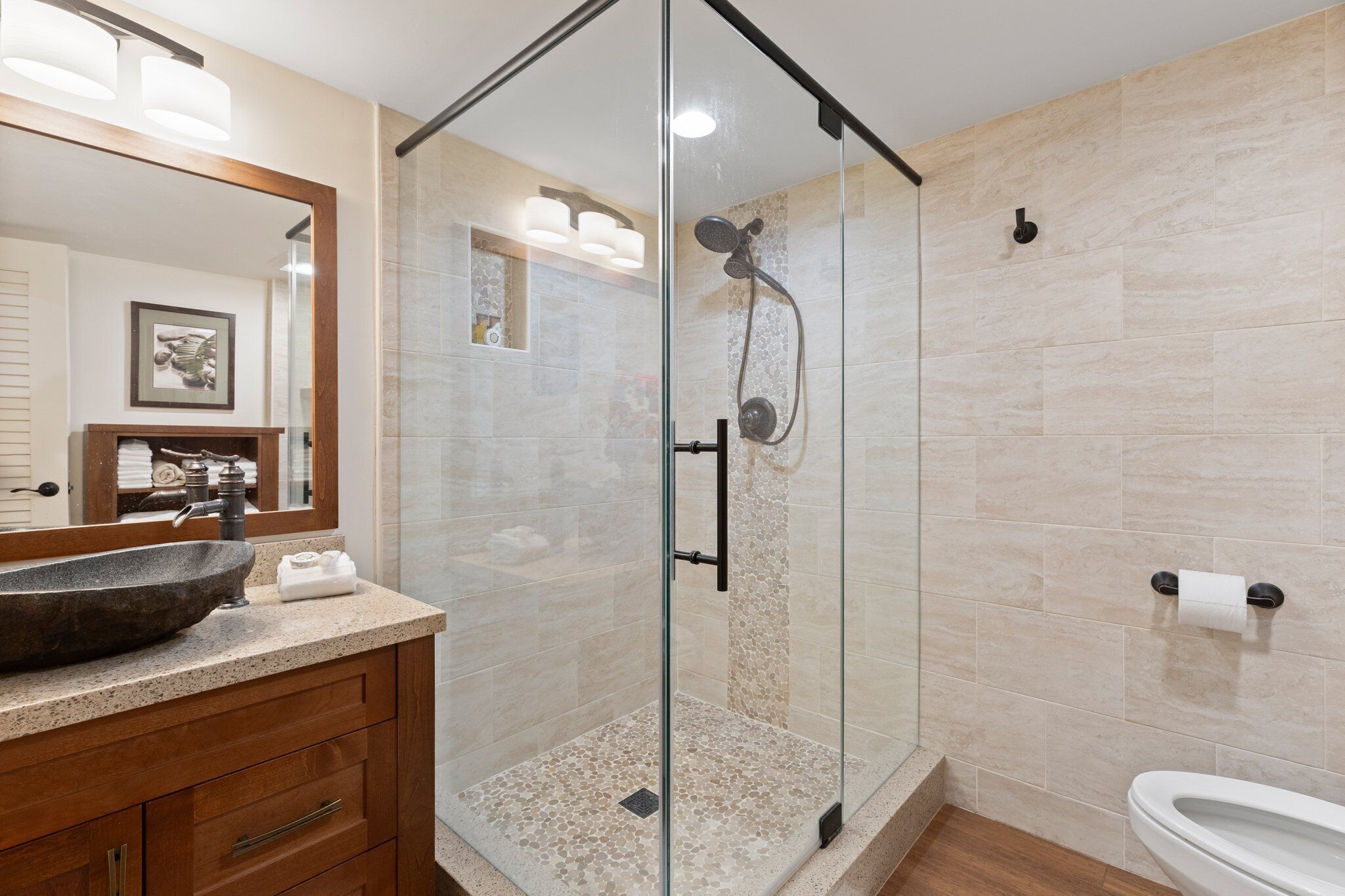 Un baño moderno con ducha de vidrio, tocador de madera con un lavamanos grande y un inodoro.
