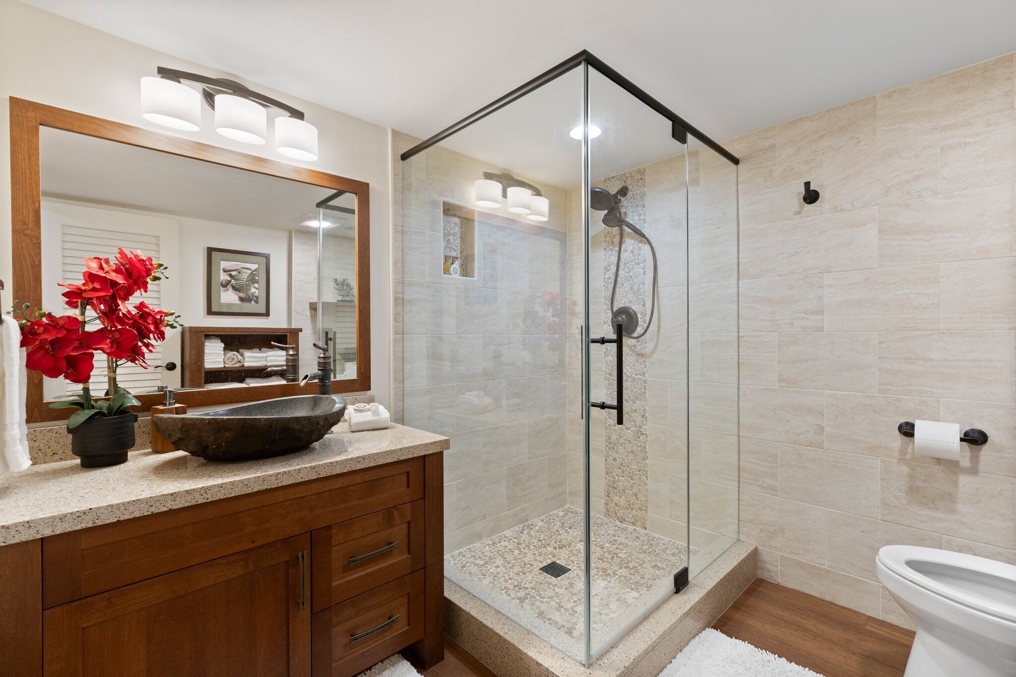 Une salle de bain moderne dotée d’une douche à parois de verre, d’un meuble-lavabo en bois avec un grand lavabo en cuvette et d’un grand miroir au-dessus du meuble-lavabo.