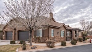 Une maison à deux étages avec une façade en pierre, un grand garage et une cour avant bien entretenue, agrémentée d’un aménagement paysager.