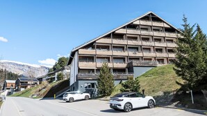 A multi-story building with a sloped roof, likely a hotel or resort, with a parking area in front. - La Prada Wohnung 119 by Interhome (Laax)