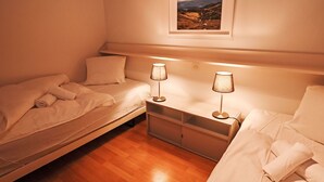 A bedroom with two single beds, a nightstand with lamps, and a framed landscape painting on the wall. - La Prada Wohnung 119 by Interhome (Laax)