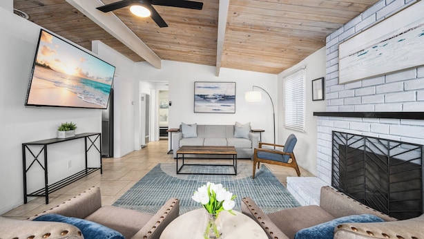 A modern living room with a fireplace, a ceiling fan, and a large painting on the wall.
