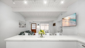 A modern kitchen with a marble countertop, white cabinetry, and a dining area with a white table and chairs.