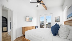 A bedroom with a bed, a ceiling fan, a wooden dresser, and a view of the outside.