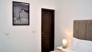 Un dormitorio con una cama, una mesita de noche con lámpara, una puerta y un cuadro en la pared.