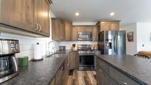 A modern kitchen with wooden cabinets, stainless steel appliances, and a granite countertop. - New! Home located off Flathead River with balcony & fireplace (Columbia Falls)