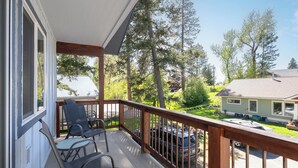 A wooden deck with two chairs and a table, overlooking a residential area with trees and a house. - New! Home located off Flathead River with balcony & fireplace (Columbia Falls)