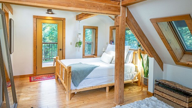 Ein Schlafzimmer mit einem hölzernen Bettgestell, einem großen Fenster und Blick ins Freie.