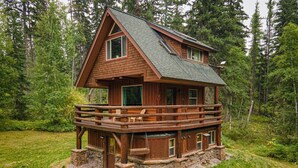 Eine Holzhütte mit Balkon, Steinfundament und Picknicktisch in einer Waldlandschaft.
