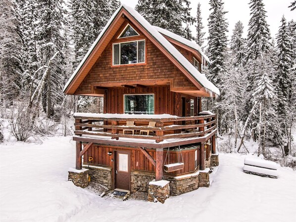 Una cabaña de madera de dos pisos con balcón, rodeada de árboles cubiertos de nieve.