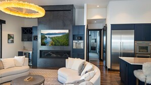 Ein modernes Wohnzimmer mit Kamin, großem Fernseher und einer Küche mit Edelstahlgeräten.