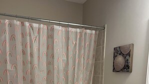 Un baño con cortina de ducha estampada con un diseño de arcoíris, un inodoro blanco y un lavamanos color beige.