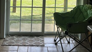 Una habitación con una puerta corrediza de vidrio que da a un patio cubierto de césped. Una silla plegable verde está colocada cerca de la puerta.