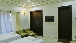 Une chambre d’hôtel avec deux lits simples, un canapé, une télévision et une armoire.