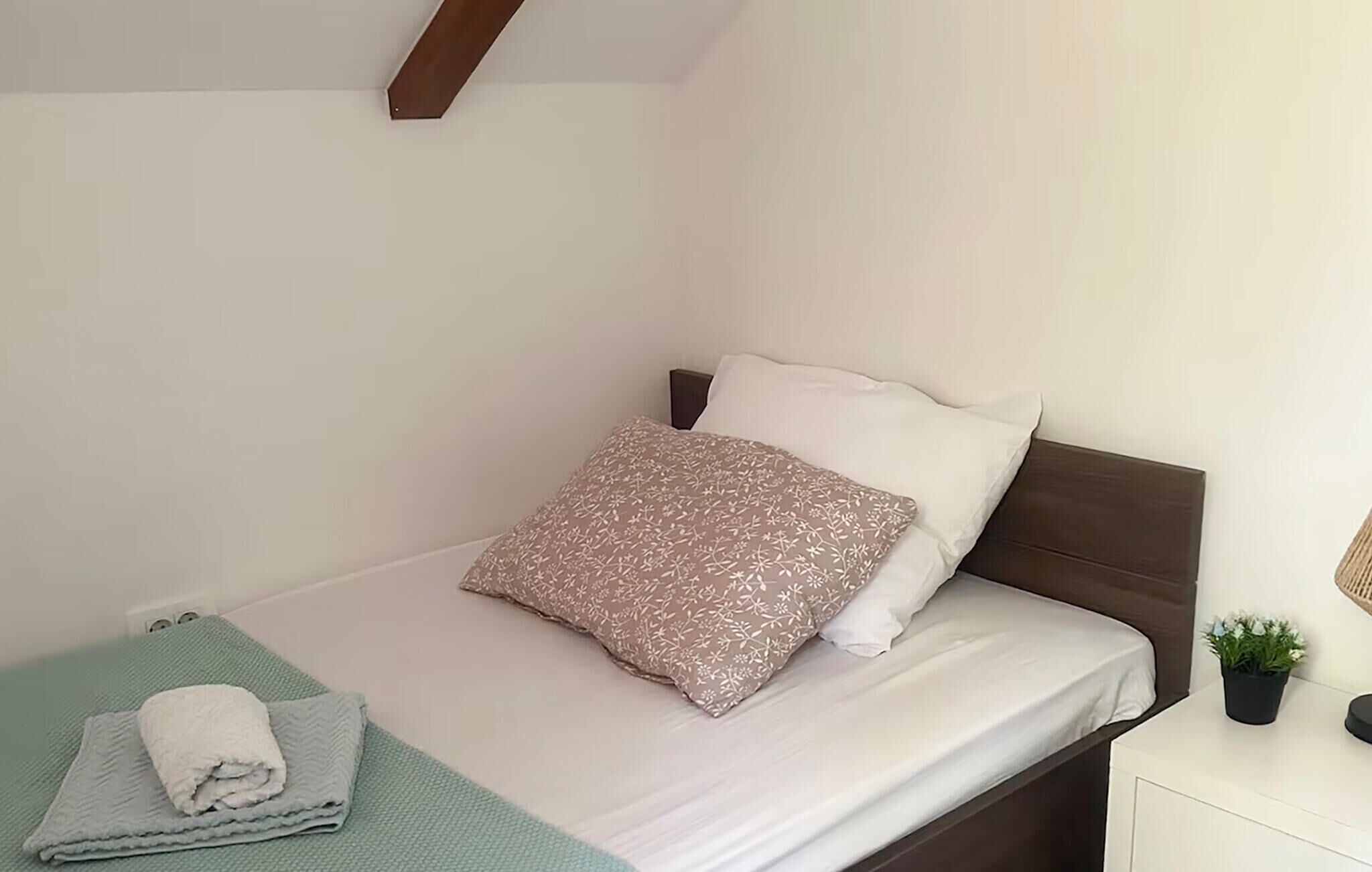 Una cama bien hecha con una almohada estampada y una toalla doblada sobre un tapete verde.