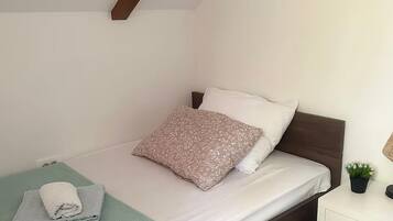 Una cama bien hecha con una almohada estampada y una toalla doblada sobre un tapete verde.