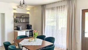 A dining area with a wooden table, green chairs, a vase of flowers, and a kitchen area with a striped cabinet and appliances. - Pet friendly home in Durdevac (Durdevac)