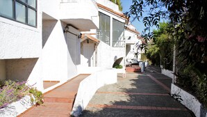 Uma passagem estreita e pavimentada que leva a um edifício branco com janelas amplas e telhado inclinado.