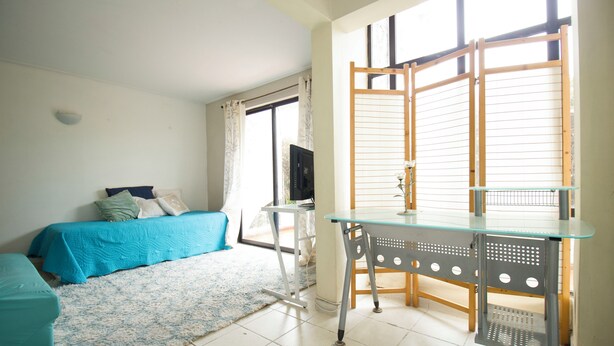 Quarto com cama, escrivaninha e janela com persianas.