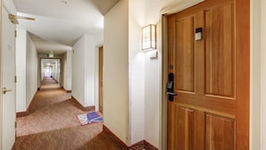 A hotel hallway with patterned carpet, wooden doors, and a light fixture. - Gateway Studio | Pool, Hot Tub, Walk to Slopes! (Keystone)