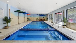 An indoor swimming pool with a blue tiled floor, surrounded by windows, potted plants, and colorful umbrellas. - Gateway Studio | Pool, Hot Tub, Walk to Slopes! (Keystone)