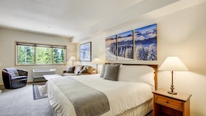 A hotel room with a large bed, two bedside tables, a chair, a window with a view of trees, and a painting on the wall. - Gateway Studio | Pool, Hot Tub, Walk to Slopes! (Keystone)