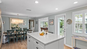 A spacious kitchen with a large island, wooden flooring, and a dining area with teal chairs.