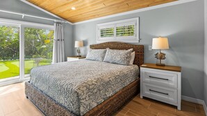 A bedroom with a large bed, two bedside tables with lamps, a window with curtains, and a view of a garden.